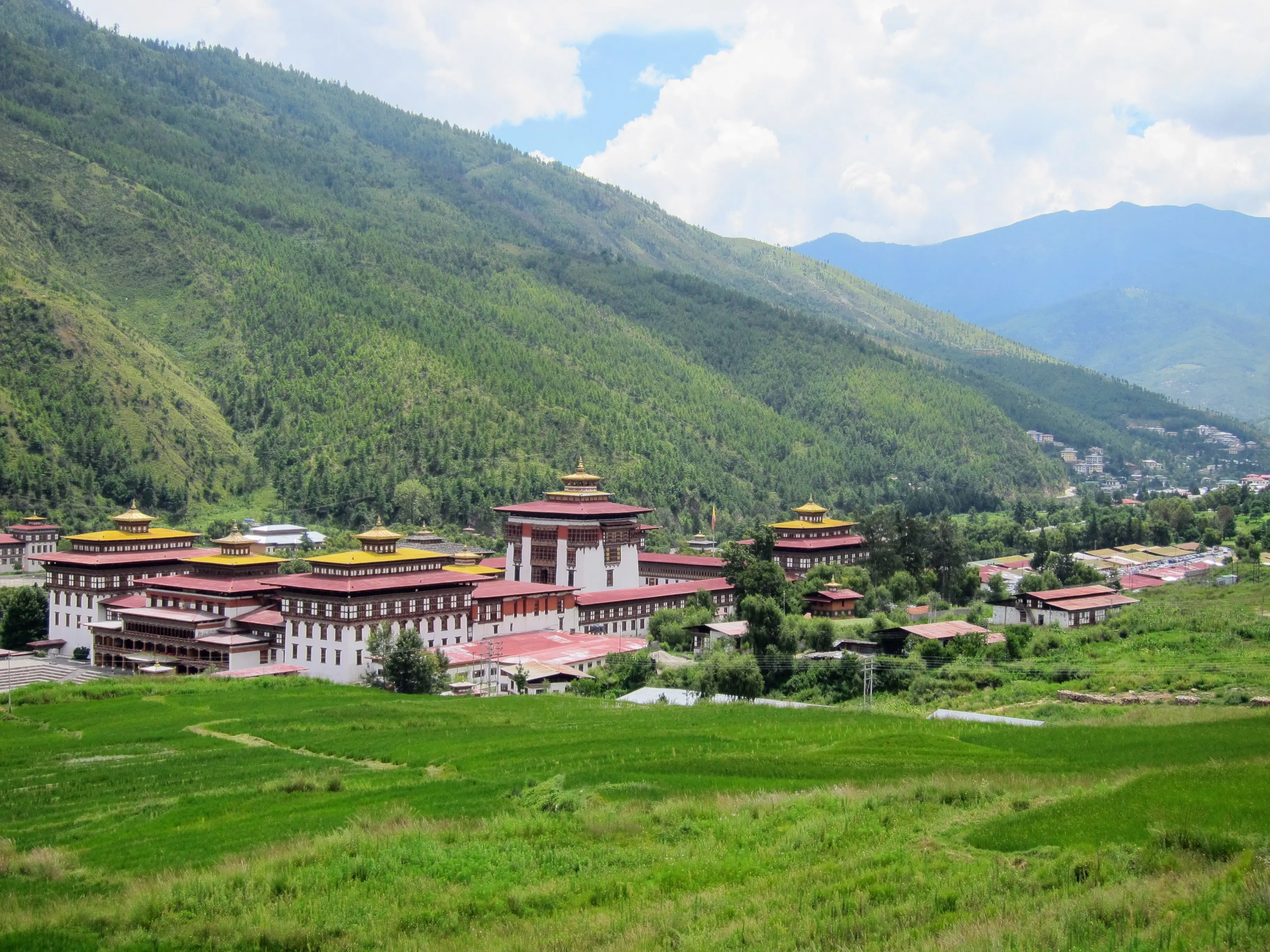 The Thimphu valley and Tashichho Dzong in monsoon green under a mixed sky