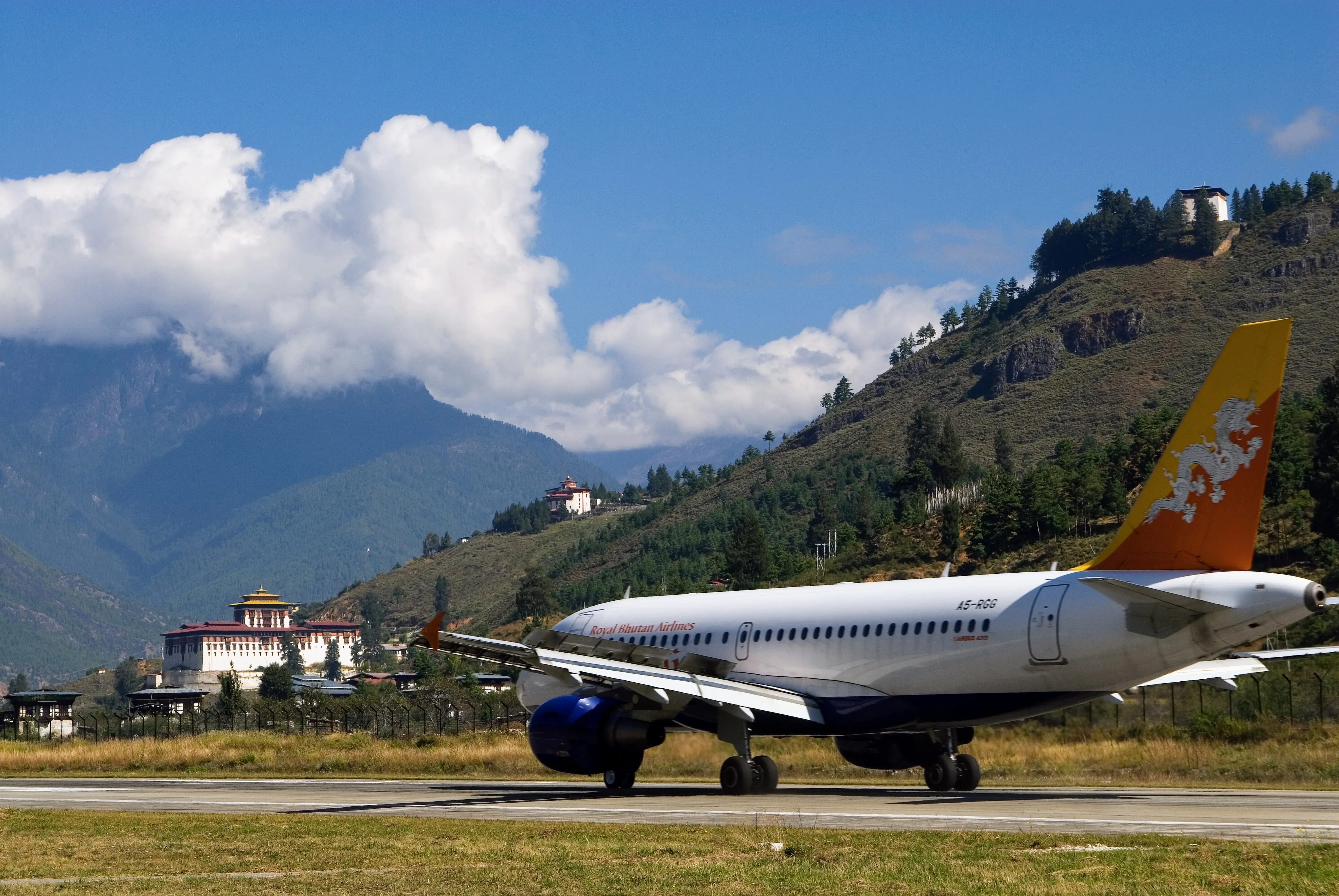 A Royal Bhutan Airlines jet on the Paro runway, Rinpung Dzong and the valley walls rising behind it