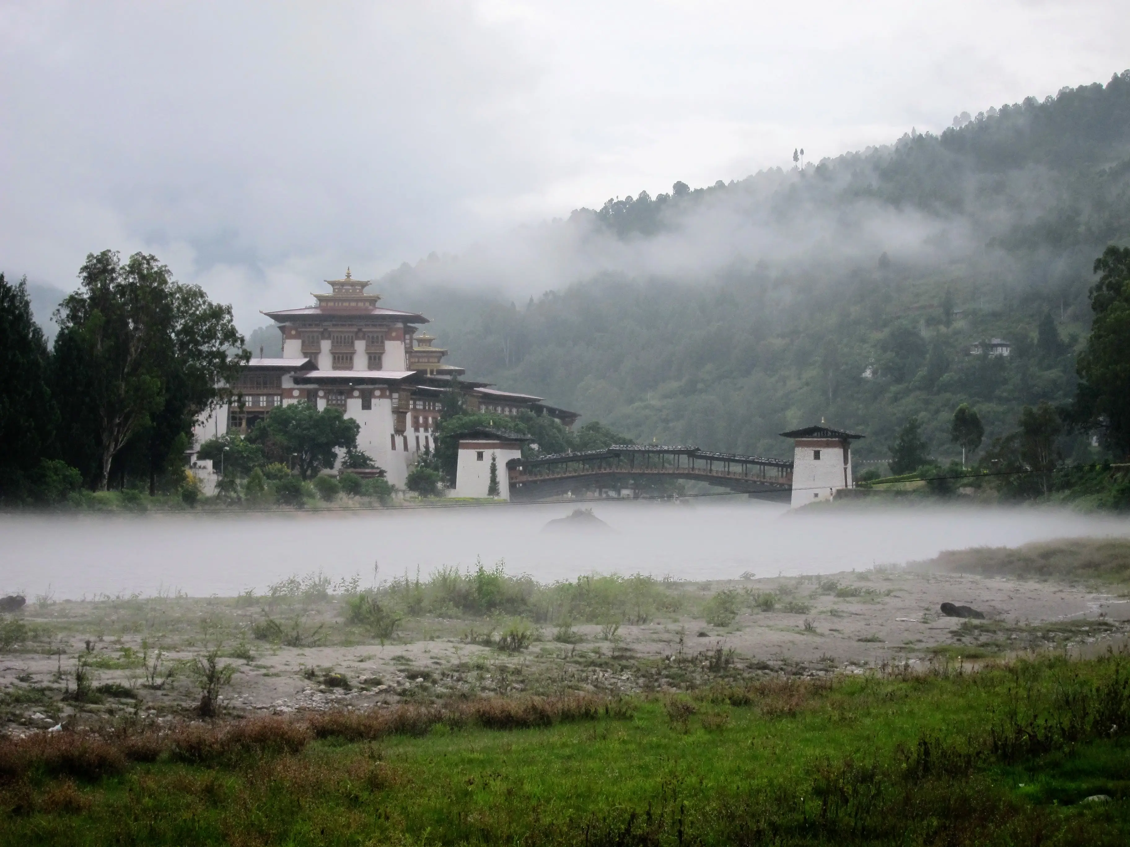 Punakha Dzong under low monsoon cloud, mist rising off the river