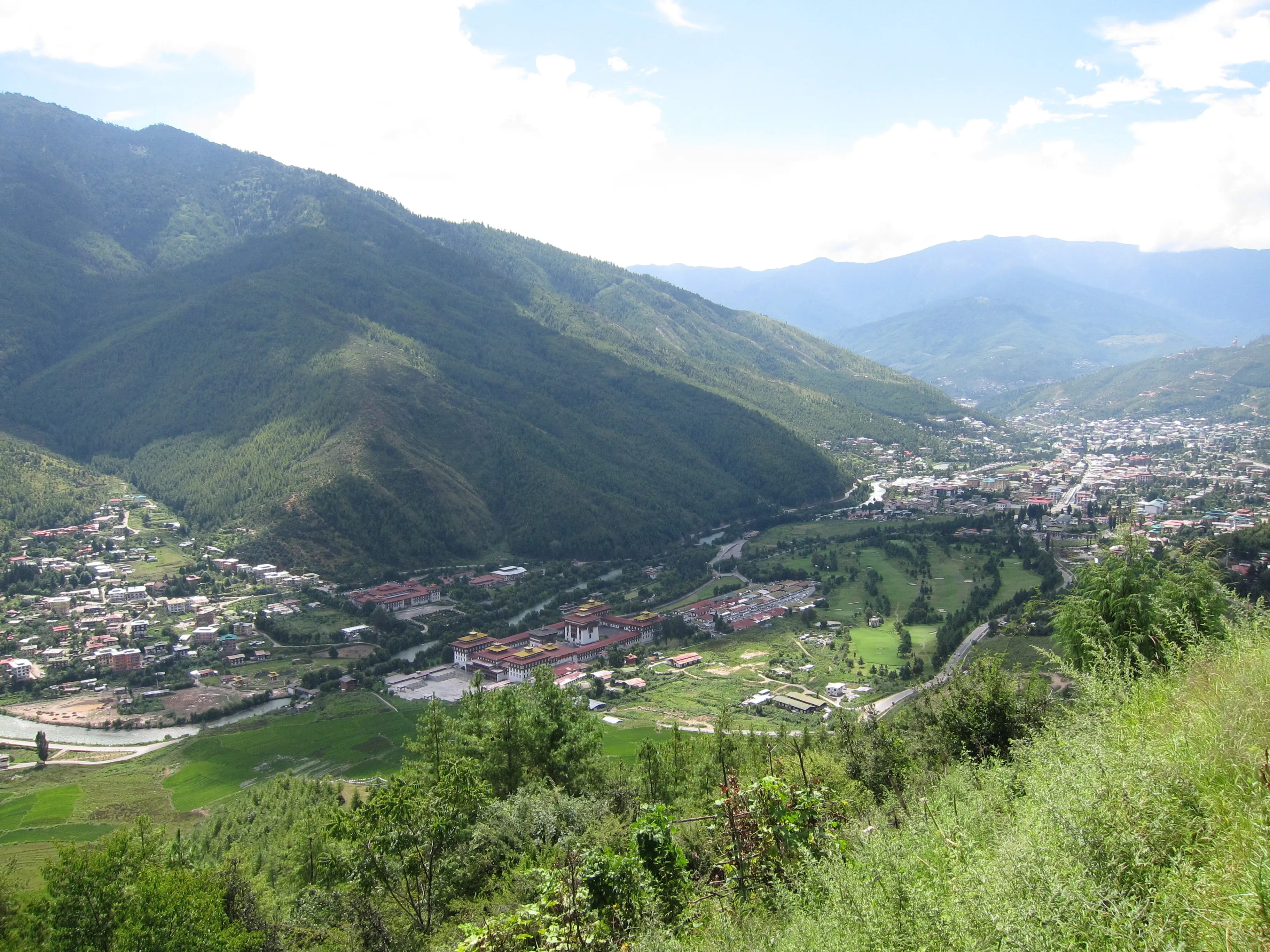 The Thimphu valley in summer green, Tashichho Dzong and the capital below forested ridges